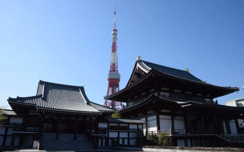 A serene view of Zojoji Temple with the iconic Tokyo Tower rising behind it under a clear sky.