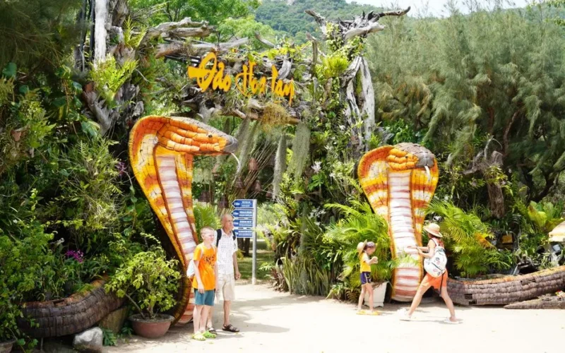 Tourists admire colorful snake sculptures at a tropical outdoor attraction, surrounded by lush greenery.