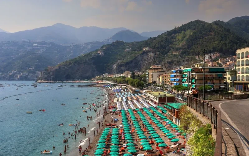 A lively summer day at Sorrento's coastline with colorful umbrellas and mountains.