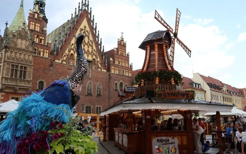 Colorful scene in Wrocław's Market Square showcasing a peacock sculpture and a festive windmill stall.