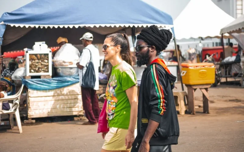 A cheerful couple enjoys a walk through a bustling market in Accra, Ghana, capturing local life and culture.