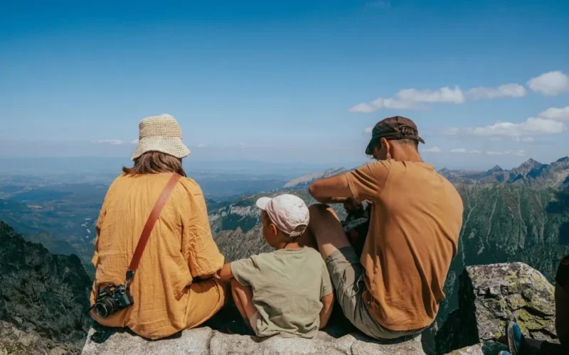 Family sitting on a rock, enjoying a panoramic view of the Tatra Mountains under clear blue skies.