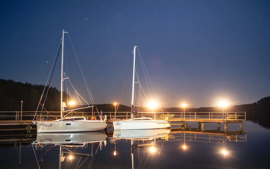 Peaceful night view of sailboats docked in Mazury, reflecting under a starry sky.