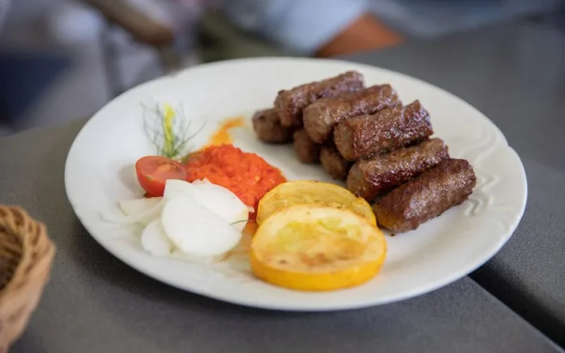 Plate of flavorful grilled cevapi with fresh vegetables and red pepper sauce. Perfect traditional Balkan meal.