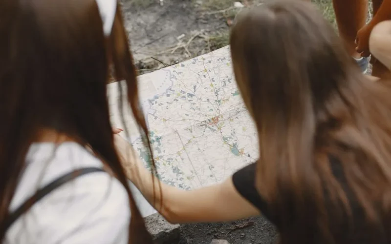 Two women study a map outdoors, planning their hiking route.